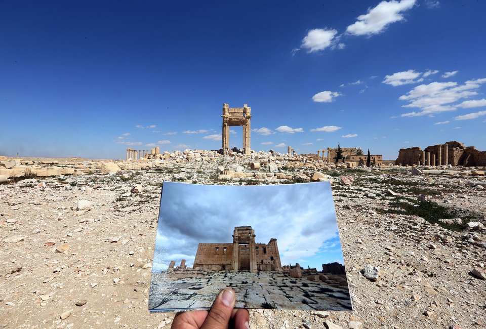 A general view taken on March 31, 2016 shows a photographer holding his picture of the Temple of Bel taken on March 14, 2014 in front of the remains of the historic temple after it was destroyed by Islamic State (IS) group jihadists in September 2015 in the ancient Syrian city of Palmyra. Syrian troops backed by Russian forces recaptured Palmyra on March 27, 2016, after a fierce offensive to rescue the city from jihadists who view the UNESCO-listed site's magnificent ruins as idolatrous. / AFP / JOSEPH EID (Photo credit should read JOSEPH EID/AFP/Getty Images)