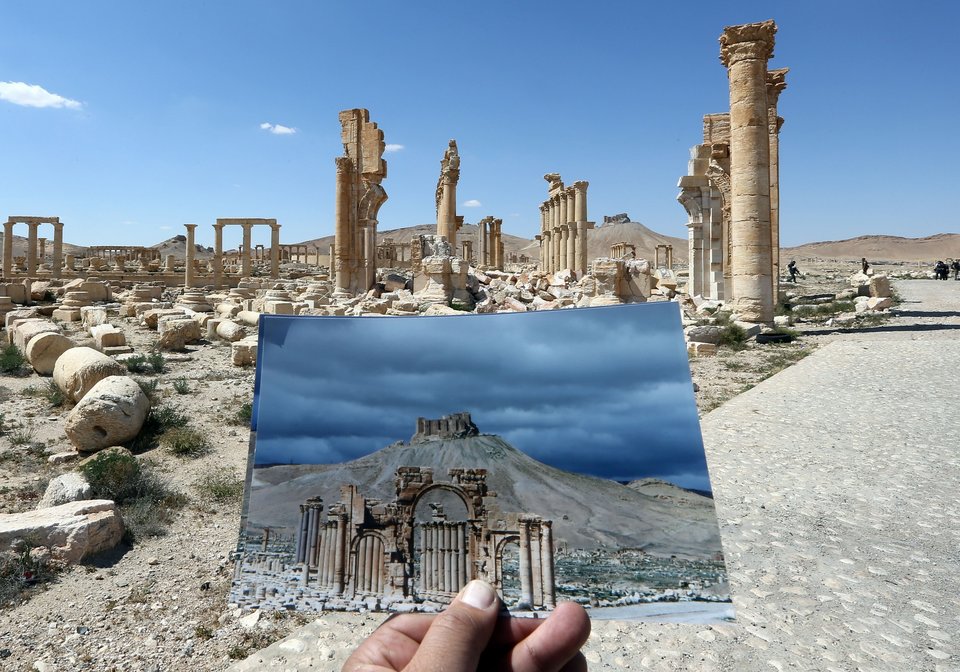 A general view taken on March 31, 2016 shows a photographer holding his picture of the Arc du Triomphe (Triumph's Arch) taken on March 14, 2014 in front of the remains of the historic monument after it was destroyed by Islamic State (IS) group jihadists in October 2015 in the ancient Syrian city of Palmyra. Syrian troops backed by Russian forces recaptured Palmyra on March 27, 2016, after a fierce offensive to rescue the city from jihadists who view the UNESCO-listed site's magnificent ruins as idolatrous. / AFP / JOSEPH EID (Photo credit should read JOSEPH EID/AFP/Getty Images)