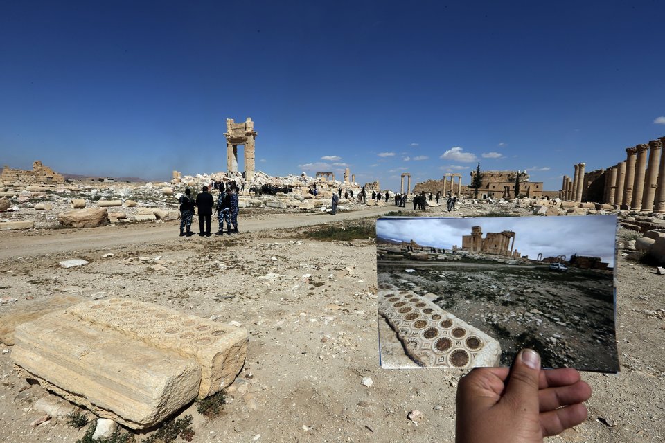 A general view taken on March 31, 2016 shows a photographer holding his picture of the Temple of Bel taken on March 14, 2014 in front of the remains (far-L) of the historic temple after it was destroyed by Islamic State (IS) group jihadists in September 2015 in the ancient Syrian city of Palmyra. Syrian troops backed by Russian forces recaptured Palmyra on March 27, 2016, after a fierce offensive to rescue the city from jihadists who view the UNESCO-listed site's magnificent ruins as idolatrous. / AFP / JOSEPH EID (Photo credit should read JOSEPH EID/AFP/Getty Images)