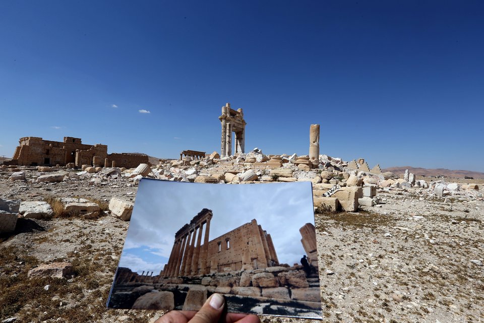 A general view taken on March 31, 2016 shows a photographer holding his picture of the Temple of Bel taken on March 14, 2014 in front of the remains of the historic temple after it was destroyed by Islamic State (IS) group jihadists in September 2015 in the ancient Syrian city of Palmyra. Syrian troops backed by Russian forces recaptured Palmyra on March 27, 2016, after a fierce offensive to rescue the city from jihadists who view the UNESCO-listed site's magnificent ruins as idolatrous. / AFP / JOSEPH EID (Photo credit should read JOSEPH EID/AFP/Getty Images)